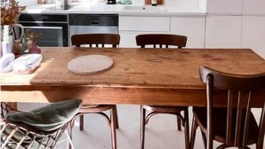 Une cuisine moderne avec des meubles blancs, une table à manger en bois et un luminaire suspendu.