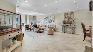 A spacious living room with a large window, a wooden coffee table, a beige sofa, and a television mounted on the wall.