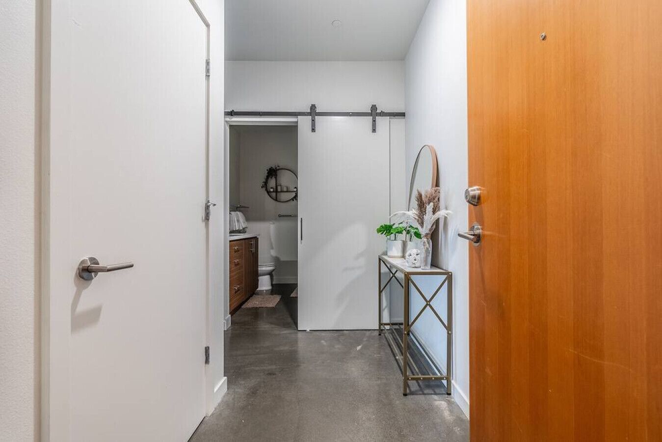 A hallway with a sliding door, a wooden door, a console table with a vase, and a mirror.