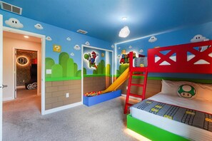 A child's playroom with a slide, a ladder, and a bed with a Mario-themed pillow.