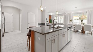 A modern kitchen with a central island, pendant lights, and a dining area with a view.