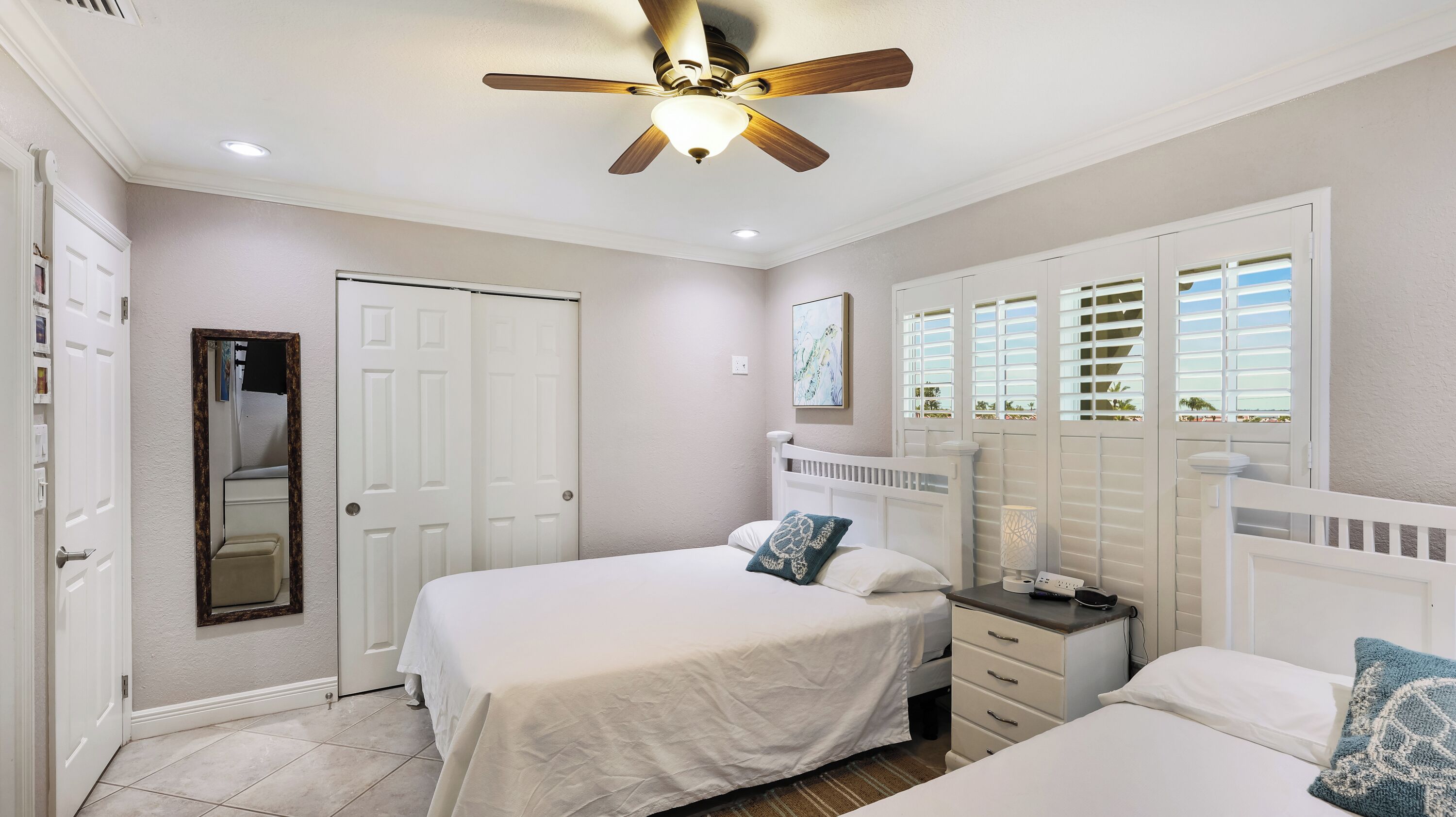 A bedroom with a ceiling fan, a bed with white bedding, a nightstand with a lamp, and a window with blinds.