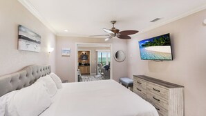 Une chambre avec un lit, un ventilateur de plafond, une télévision et une vue sur l’océan, accessible par une porte coulissante.