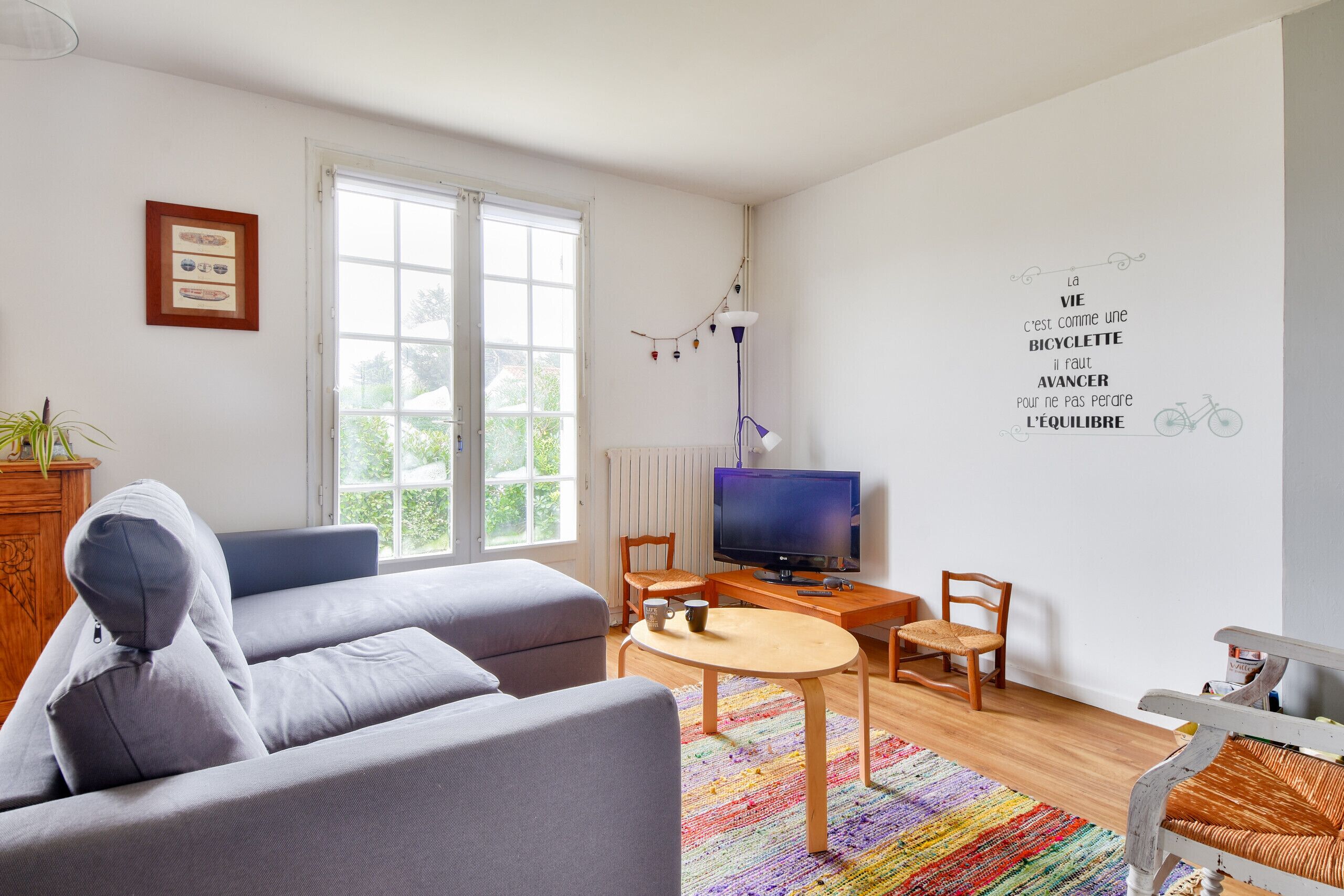 Un salon comprenant un canapé, un téléviseur, une table basse et un mur orné d’une citation inspirante.