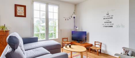 Un salon comprenant un canapé, un téléviseur, une table basse et un mur orné d’une citation inspirante.