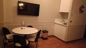 A small dining area with a round table and four chairs, a television mounted on the wall, and a white cabinet with a sink. - MARAIS LOVELY BEAUBOURG A (Paris)