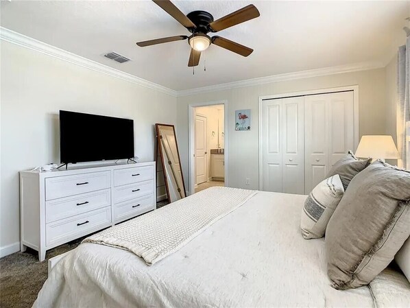 A bedroom with a bed, a dresser, a television, a ceiling fan, and a door.