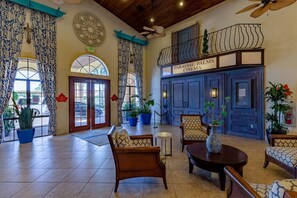 Un vestíbulo con un amplio ventanal de arco, una recepción y una zona de estar con sillas estampadas y una mesa.