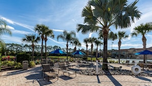 An outdoor patio area with lounge chairs and umbrellas, surrounded by palm trees and a brick walkway. - Last Minute Disney Getaway! Townhouse with Private Pool. Book Now! #101725 (Orlando)