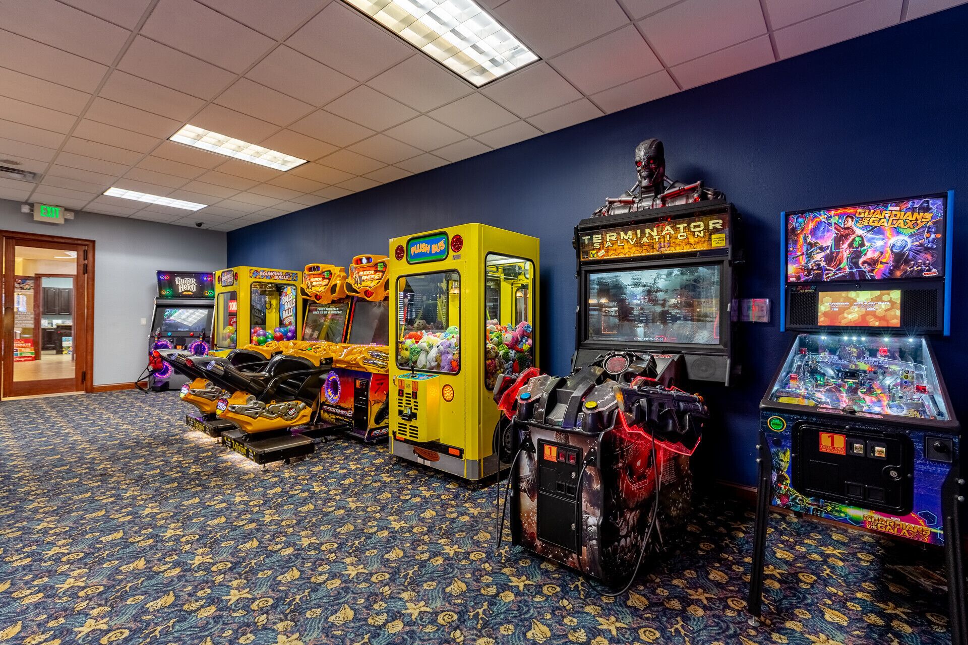 A row of arcade machines in a room with patterned carpet and a blue wall.