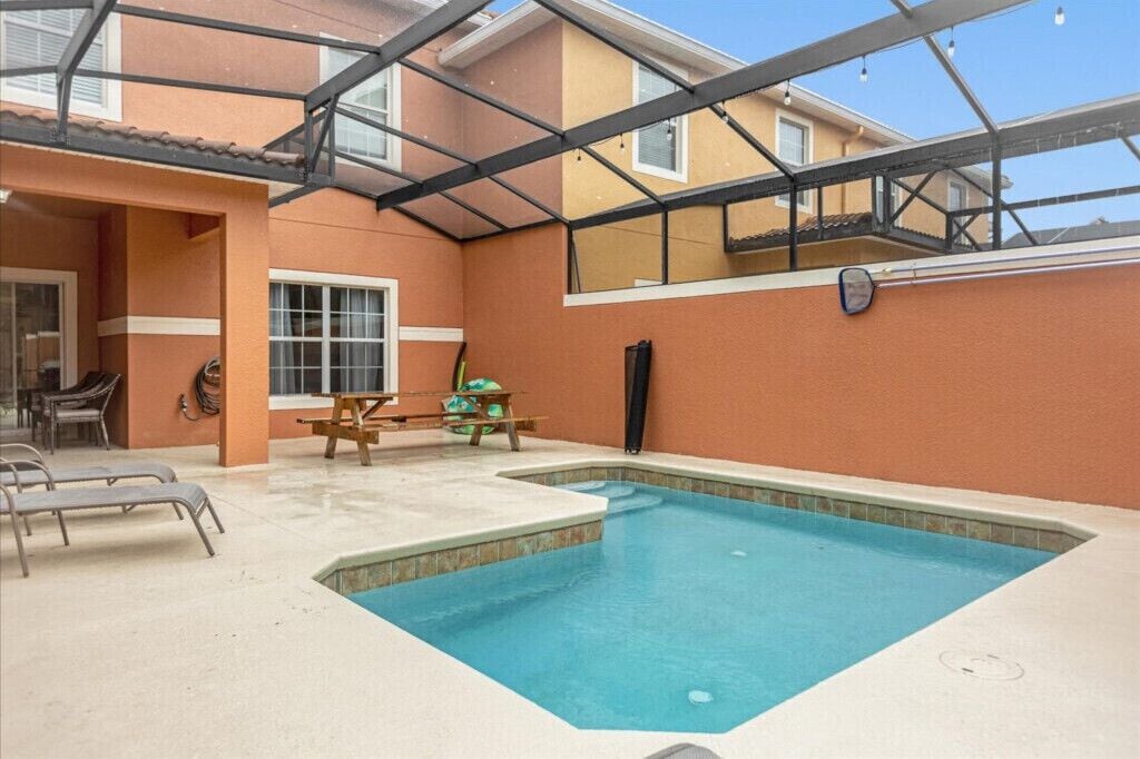 A swimming pool with lounge chairs, a wooden table, and a covered patio area.