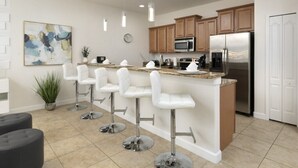 A modern kitchen with a central island, bar stools, stainless steel appliances, and pendant lighting.