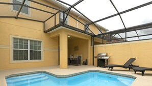 An indoor swimming pool with a glass ceiling, a barbecue grill, and lounge chairs.