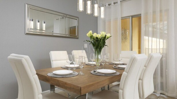 A dining room with a wooden table, white chairs, a vase of flowers, and a mirror on the wall.