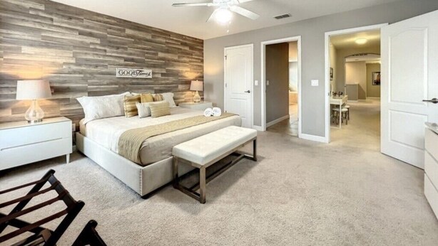 A bedroom with a bed, bedside tables, a bench, a ceiling fan, and a wall with a wood panel design.