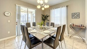 A dining area with a glass table, black chairs, a potted plant, and a clock on the wall.