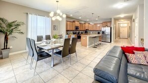 A modern kitchen with a central island, dining area with chairs, and a living room with a sofa.
