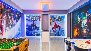 Una habitación con mesa de futbolín, mesa de billar y paredes decoradas con carteles de películas de superhéroes.