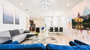 A modern living room with a sofa, coffee table, and a painting of a mountain landscape. - Last Minute Disney! Private Pool, Hot Tub & Themed Bedrooms. Book Now! #106587 (Orlando)