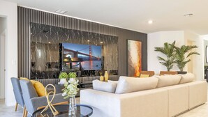 A modern living room with a large flat-screen TV, a beige sofa, and a glass coffee table. - Last Minute Disney! Private Pool, Hot Tub, Game Room & Themed Bedrooms. Book Now! #107763 (Orlando)