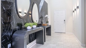 A modern reception area with a marble wall, a large mirror, and a bench with potted plants. - Last Minute Disney! Private Pool, Hot Tub, Game Room & Themed Bedrooms. Book Now! #107763 (Orlando)