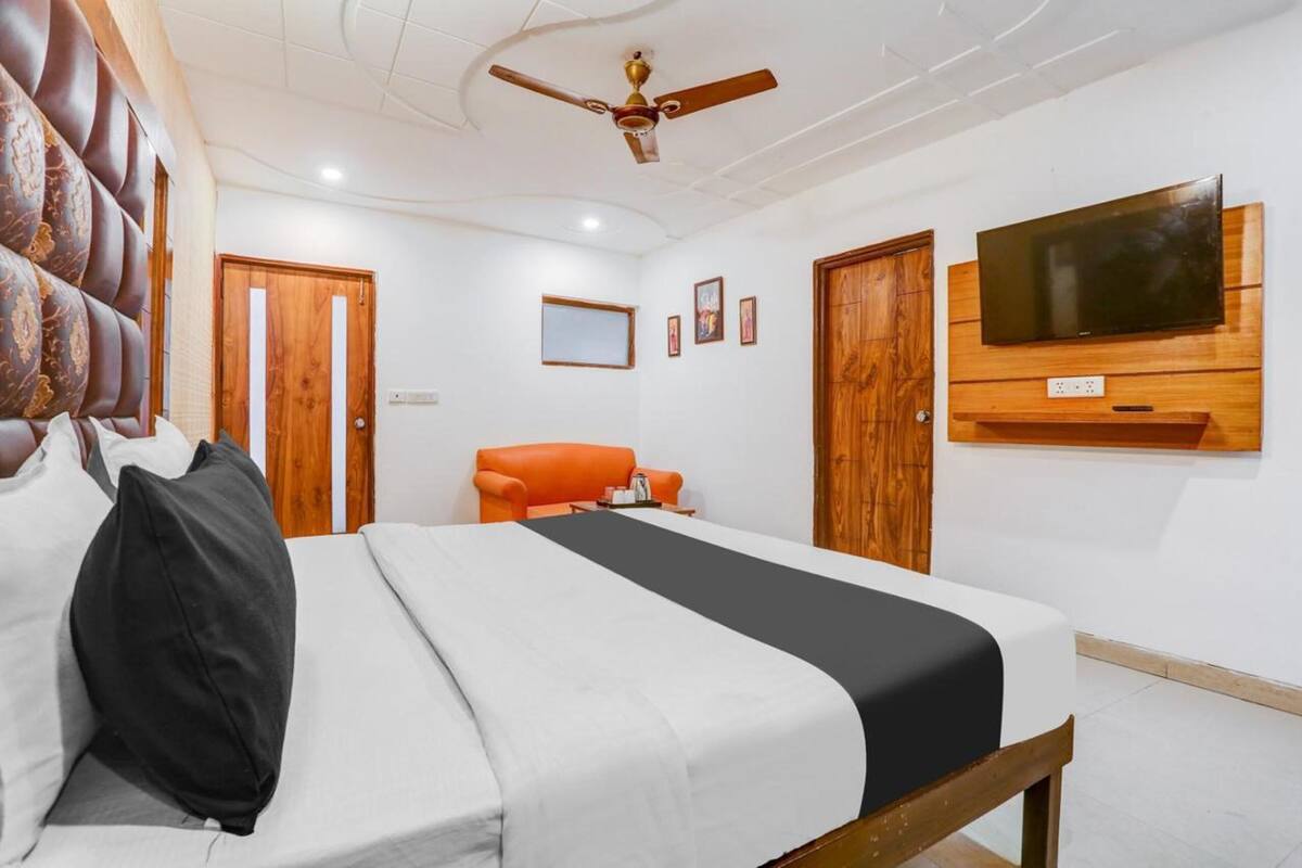 A hotel room with a bed, a sofa, a television mounted on the wall, and a ceiling fan.