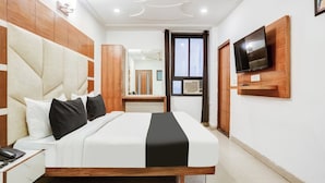 A modern hotel room with a large bed, wooden headboard, a flat-screen TV mounted on the wall, and a small desk with a telephone.