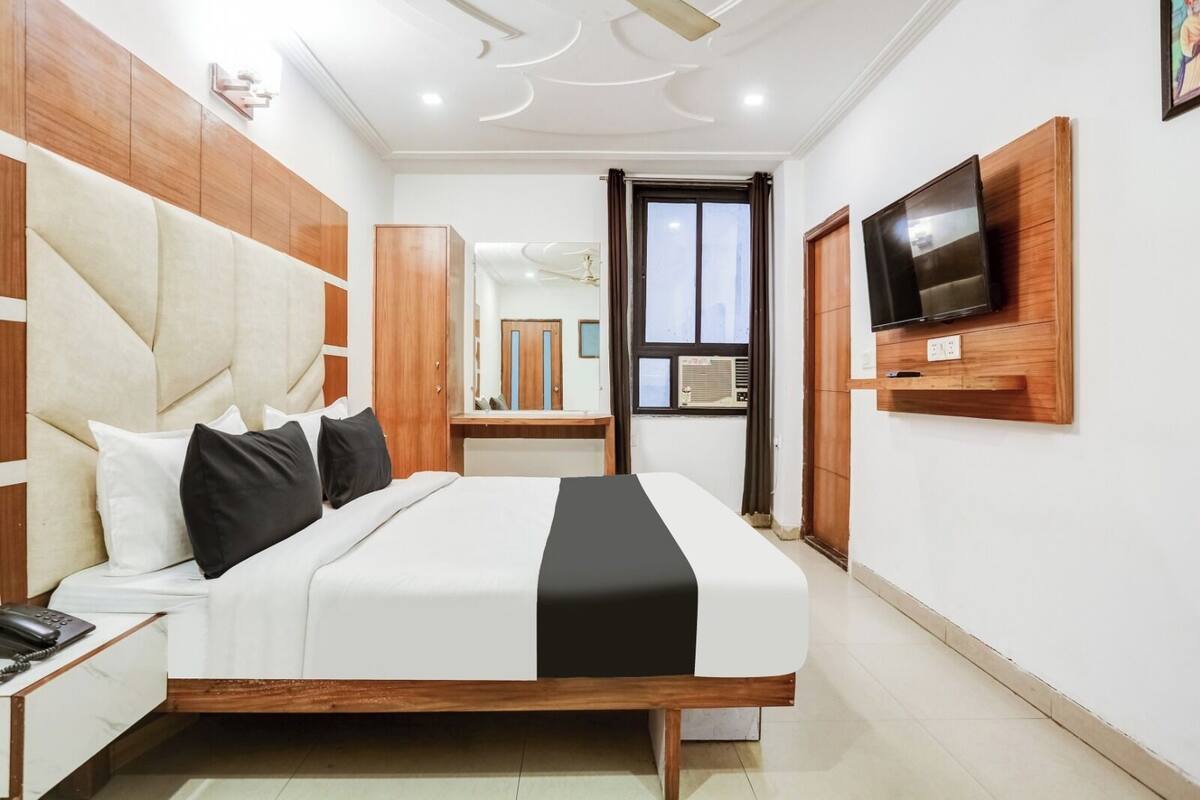 A modern hotel room with a large bed, wooden headboard, a flat-screen TV mounted on the wall, and a small desk with a telephone.