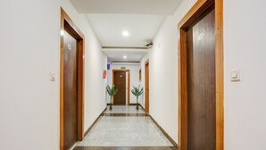 A hotel corridor with wooden doors, a marble floor, and potted plants.
