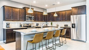 A modern kitchen with dark wood cabinets, stainless steel appliances, a granite countertop, and bar stools. - Last Minute Disney! Private Pool, Hot Tub, Game Room & Themed Bedrooms. Book Now! #107907 (Orlando)