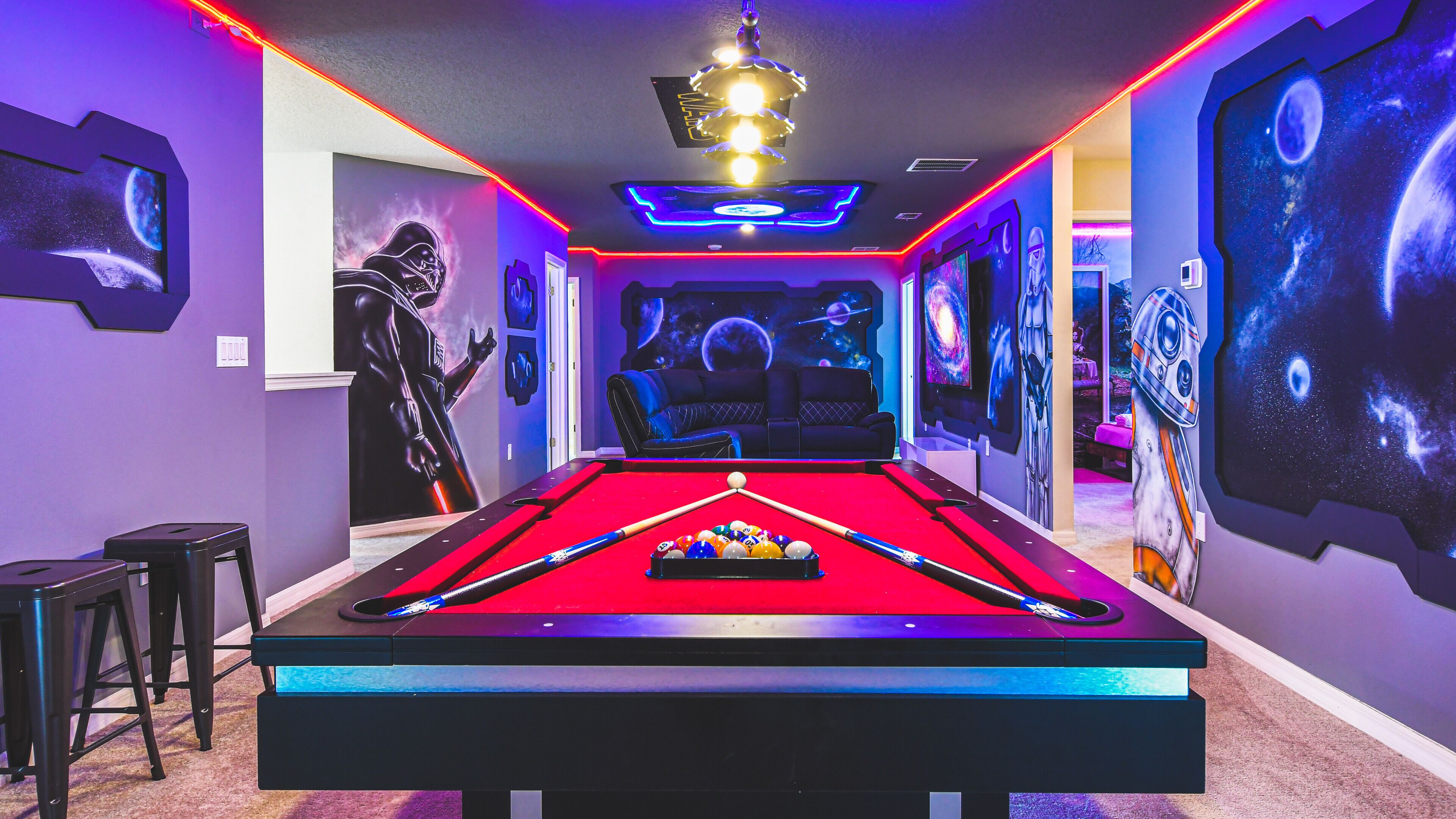 Een pooltafel met een rode viltbekleding, omringd door muren met ruimtethema muurschilderingen en LED-verlichting.