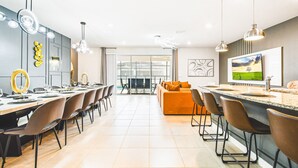A modern kitchen with a dining area, featuring a large island, bar stools, and a TV mounted on the wall. - Last Minute Disney! Private Pool, Hot Tub, Game Room & Themed Bedrooms. Book Now! #107907 (Orlando)