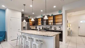 A modern kitchen with a central island, bar stools, stainless steel appliances, and pendant lighting.