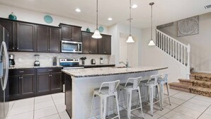 A modern kitchen with dark cabinets, a central island with bar stools, stainless steel appliances, and pendant lighting.
