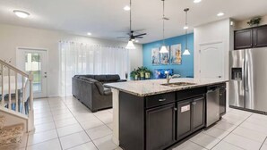 A modern kitchen with a central island, black cabinetry, stainless steel appliances, and pendant lighting.
