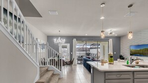 A modern kitchen with a central island, a dining area with chairs, and a staircase with a railing. - Last Minute Disney Getaway! Private Pool & Themed Bedrooms. Book Now! #65761 (Orlando)