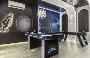 Uma mesa de bilhar com um mural com tema espacial, um moderno aparelho de ar condicionado e um lustre de cristal pendurado.