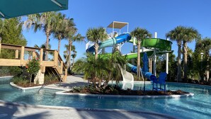 A pool area with a water slide, palm trees, and a wooden bridge.