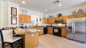 A modern kitchen with wooden cabinets, stainless steel appliances, a granite countertop, and a dining area with a chair. - Last Minute Disney! Private Pool, Hot Tub, Game Room & Themed Bedrooms. Book Now! #91511 (Orlando)