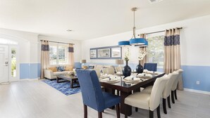 A dining area with a dark wooden table set for six, surrounded by beige upholstered chairs. There are two blue pendant lights above the table, and a blue rug on the floor. - Last Minute Disney! Private Pool, Hot Tub, Game Room & Themed Bedrooms. Book Now! #91511 (Orlando)