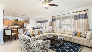 A spacious living room with a sectional sofa, a patterned armchair, and a coffee table. There is a kitchen area with wooden cabinets and a microwave. - Last Minute Disney! Private Pool, Hot Tub, Game Room & Themed Bedrooms. Book Now! #91511 (Orlando)