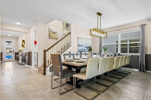 A dining area with a long table, chairs, and a chandelier. - Last Minute Disney! Private Pool, Hot Tub & Themed Bedrooms. Book Now! #91755 (Orlando)
