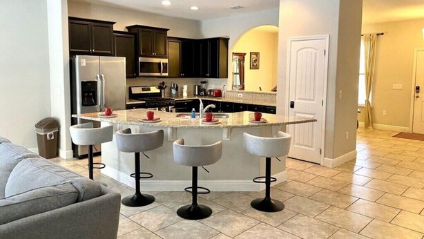 Una cocina moderna con armarios oscuros, una isla central con taburetes y electrodomésticos como refrigerador y microondas.