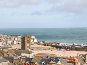 Un pueblo costero con edificios históricos, una torre de iglesia destacada y una playa de arena con barcos.