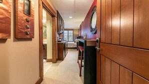 A hallway with wooden paneling, a kitchen area with a dining table, and a large mirror on the wall. - Catamount Lodge 305A - Village Junior Studio (Truckee)