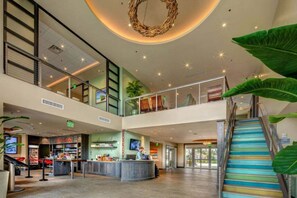 Experience the hotel's inviting lobby with a high ceiling, central open area, and a staircase leading to an upper level.