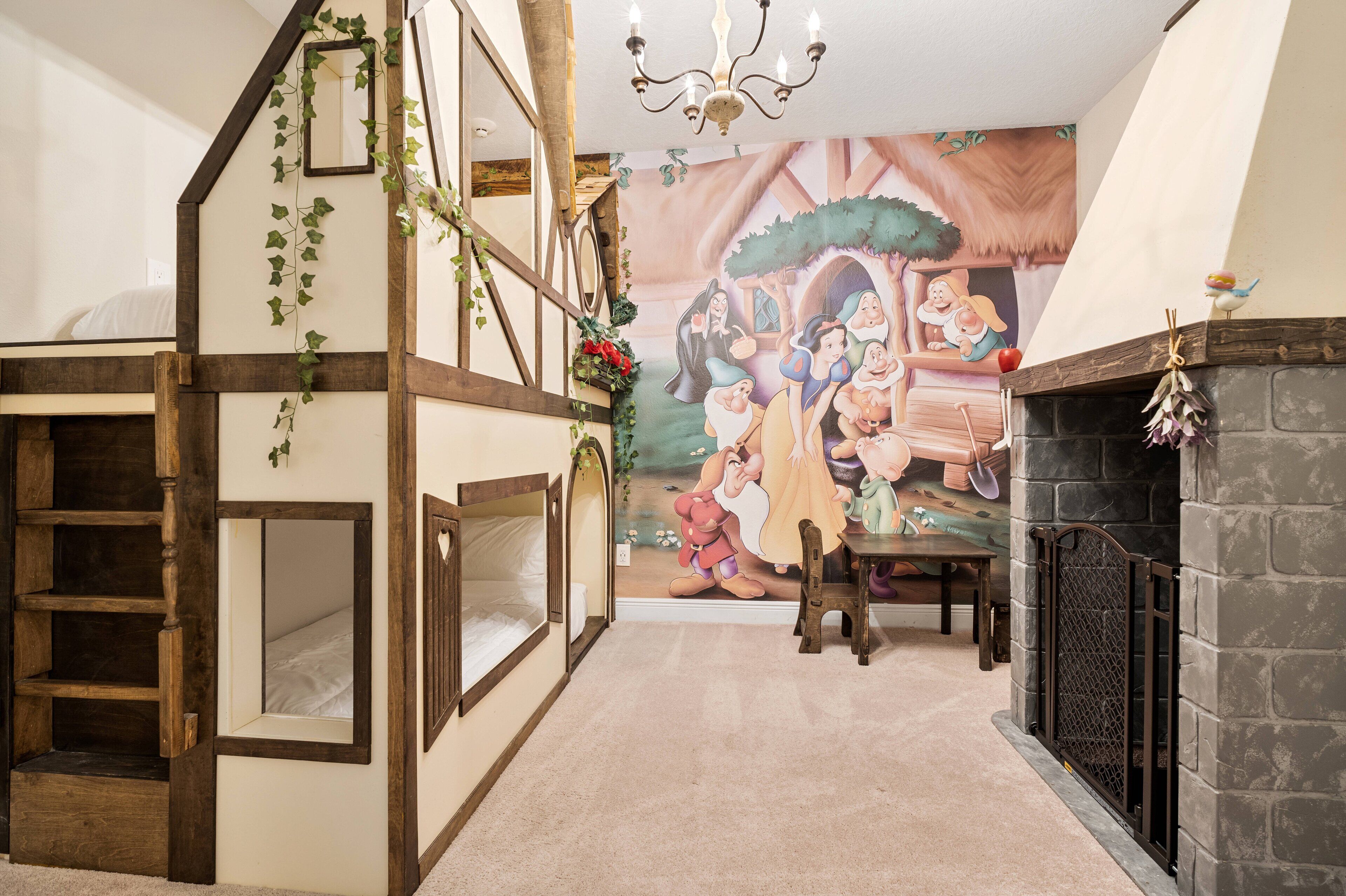 Une pièce avec un plafond haut, un lustre, une fresque représentant des personnages de dessins animés, une cheminée et une structure de jeu pour enfants.