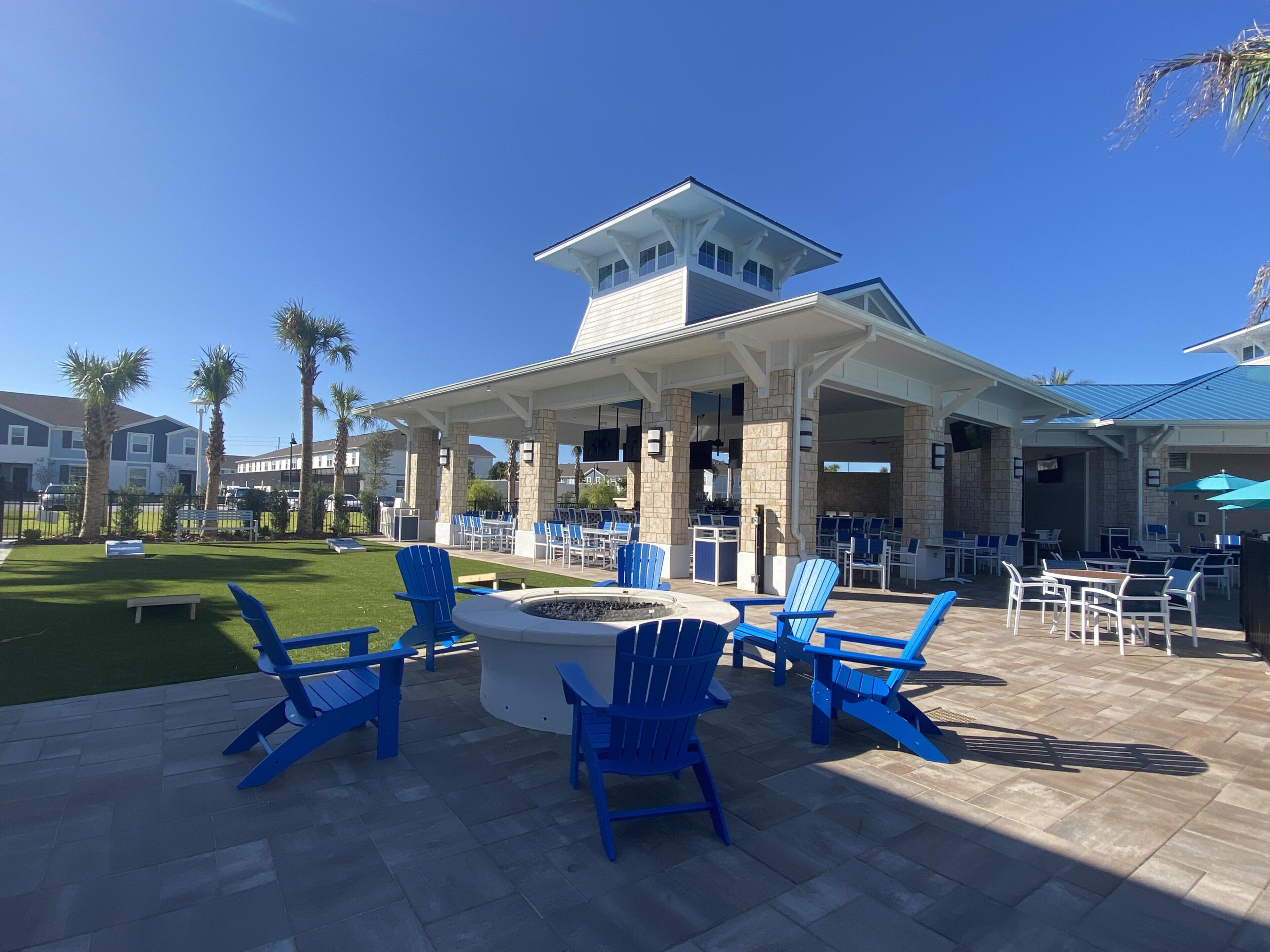 A covered outdoor seating area with blue Adirondack chairs and a fire pit, surrounded by stone pillars and a stone roof structure.