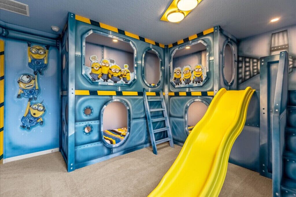 Une salle de jeux avec un toboggan jaune, des décorations sur le thème des Minions et une échelle.