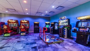 Una stanza con cabinati arcade, un tavolo da biliardo e una grande televisione.